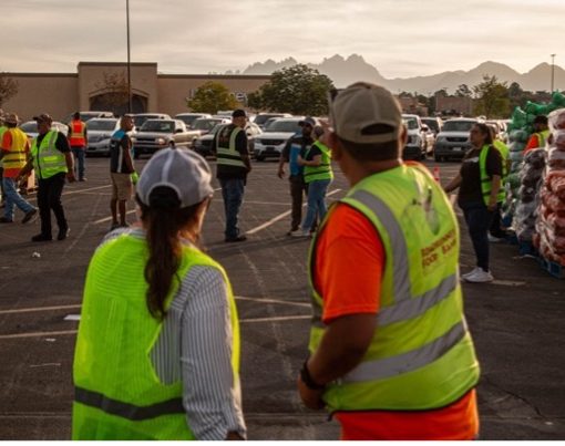 Two volunteers in safety neon vests point at other volunteers assisting at a Hunger Action Month food distribution event, as long lines of cars wait behind them at the Mesilla Valley Mall parking lot in Las Cruces, New Mexico, Saturday, Sept. 19, 2026. / Isabel Laulhé